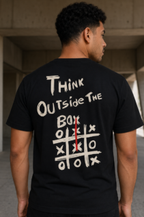 Rückansicht eines Mannes in schwarzem T-Shirt mit dem Schriftzug „Think Outside the Box“, aufgenommen in einem modernen Beton-Gang.