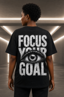 Person von hinten trägt ein schwarzes Focus Your Goal T-Shirt mit weißem Augenmotiv und grunge Grafik in einem modernen Flur.