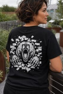 Frau mit kurzem Haar trägt ein schwarzes T-Shirt mit großem Bärenmotiv auf dem Rücken, seitlich gedreht in einem grünen Außenbereich.