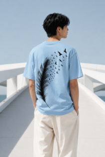 Mann von hinten trägt ein hellblaues T-Shirt mit schwarzem Feder- und Vogeldesign auf einer weißen Brücke am Meer, minimalist shirt