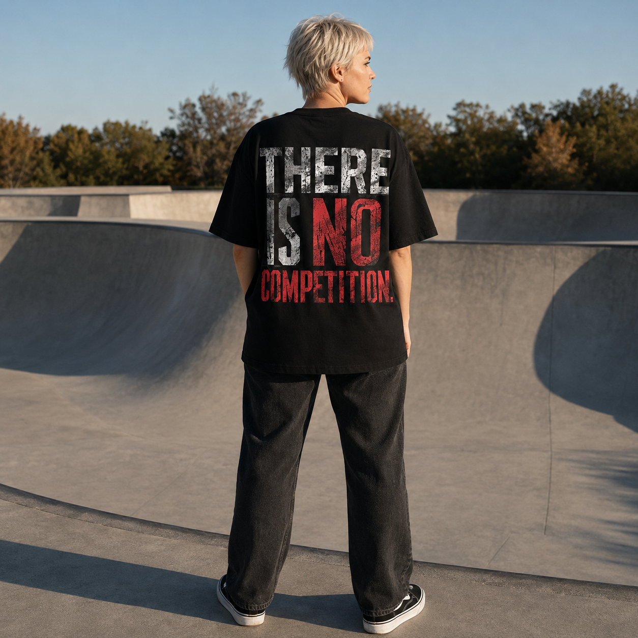 Kurzhaarige Person von hinten in schwarzem Statement T-Shirt mit rotem und weißem Aufdruck „THERE IS NO COMPETITION.“ auf einer Skatepark-Rampe.