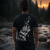 Dunkles Wolf T-Shirt mit weißem Wolf-Motiv auf dem Rücken; eine Person steht am Fluss bei Sonnenuntergang vor Wald und Felsen.