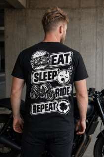 Mann von hinten trägt ein schwarzes T-Shirt mit Eat Sleep Ride-Motiv neben einem schwarzen Motorrad in einer Betongarage, lässiger Biker-Lifestyle
