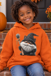 Kind in orangefarbenem Hoodie mit Hexenkatze-Motiv auf den Stufen vor einer herbstlich dekorierten Haustür, Kürbisse und schwarze Deko im Hintergrund