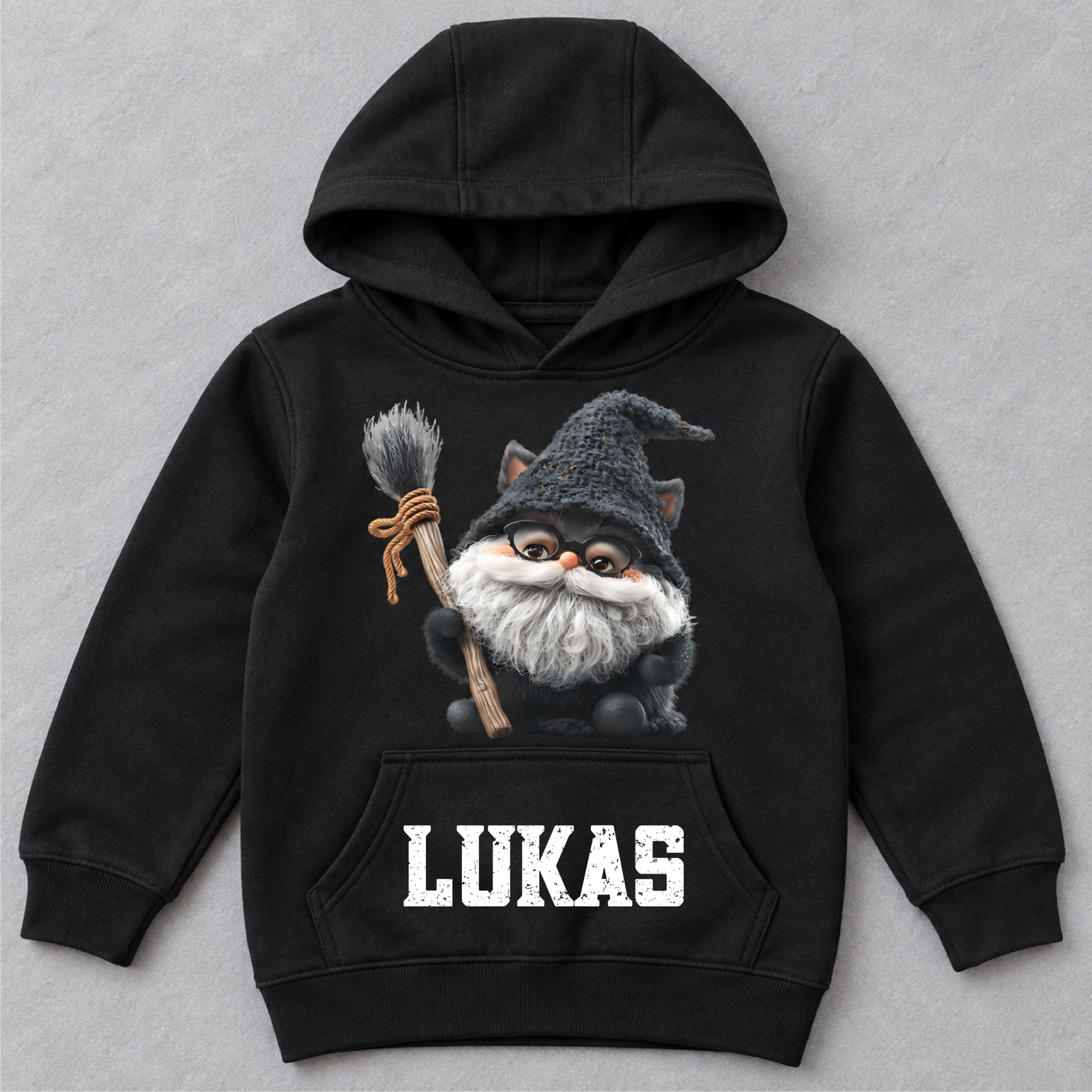 Schwarzer Kinder-Hoodie mit Hexenkatze-Motiv und dem Namen LUKAS liegt flach auf grauem Hintergrund