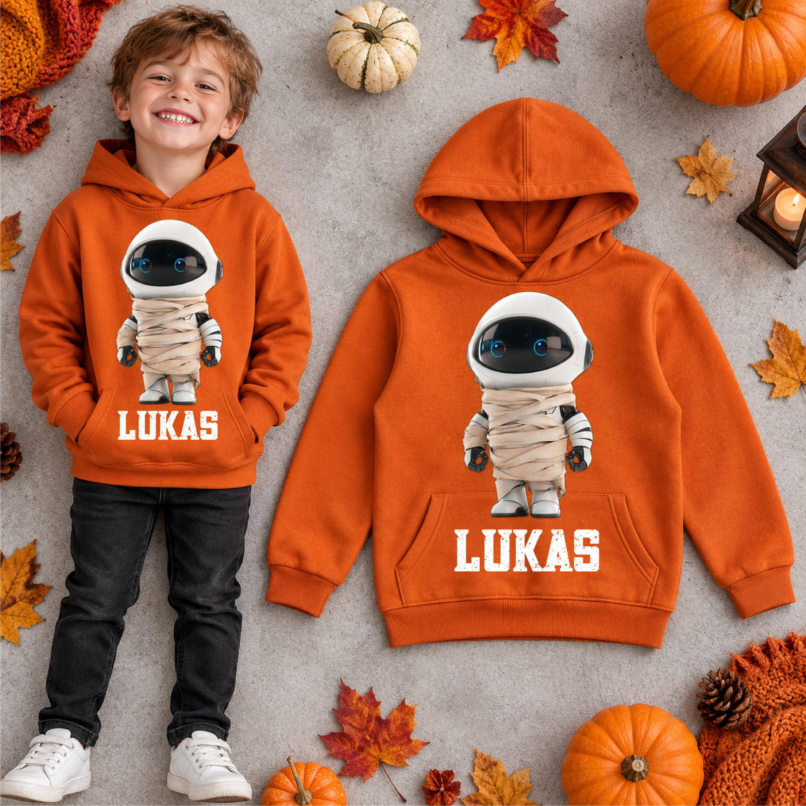 Personalisierter orangefarbener Hoodie mit Mumien-Astronaut-Motiv und Name Lukas, neben einem getragenen Kinderoutfit auf neutralem Hintergrund.