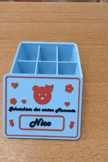 3D-gedruckte personalisierte Schatzkiste in Hellblau mit rotem Teddy und Name Nico, offen auf Holztisch mit sichtbaren Innenfächern.