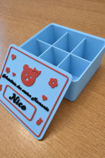 Offene personalisierte Schatzkiste aus 3D-Druck in Hellblau mit rotem Deckel und Name Nico, Innenfächer deutlich sichtbar auf Holztisch.