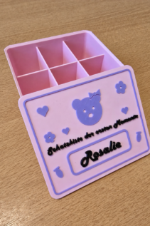 3D-gedruckte personalisierte Schatzkiste in Rosa und Lila, schräg von oben offen dargestellt, mit Teddy-Deko, Herzchen und Name Rosalie auf dem Deckel.